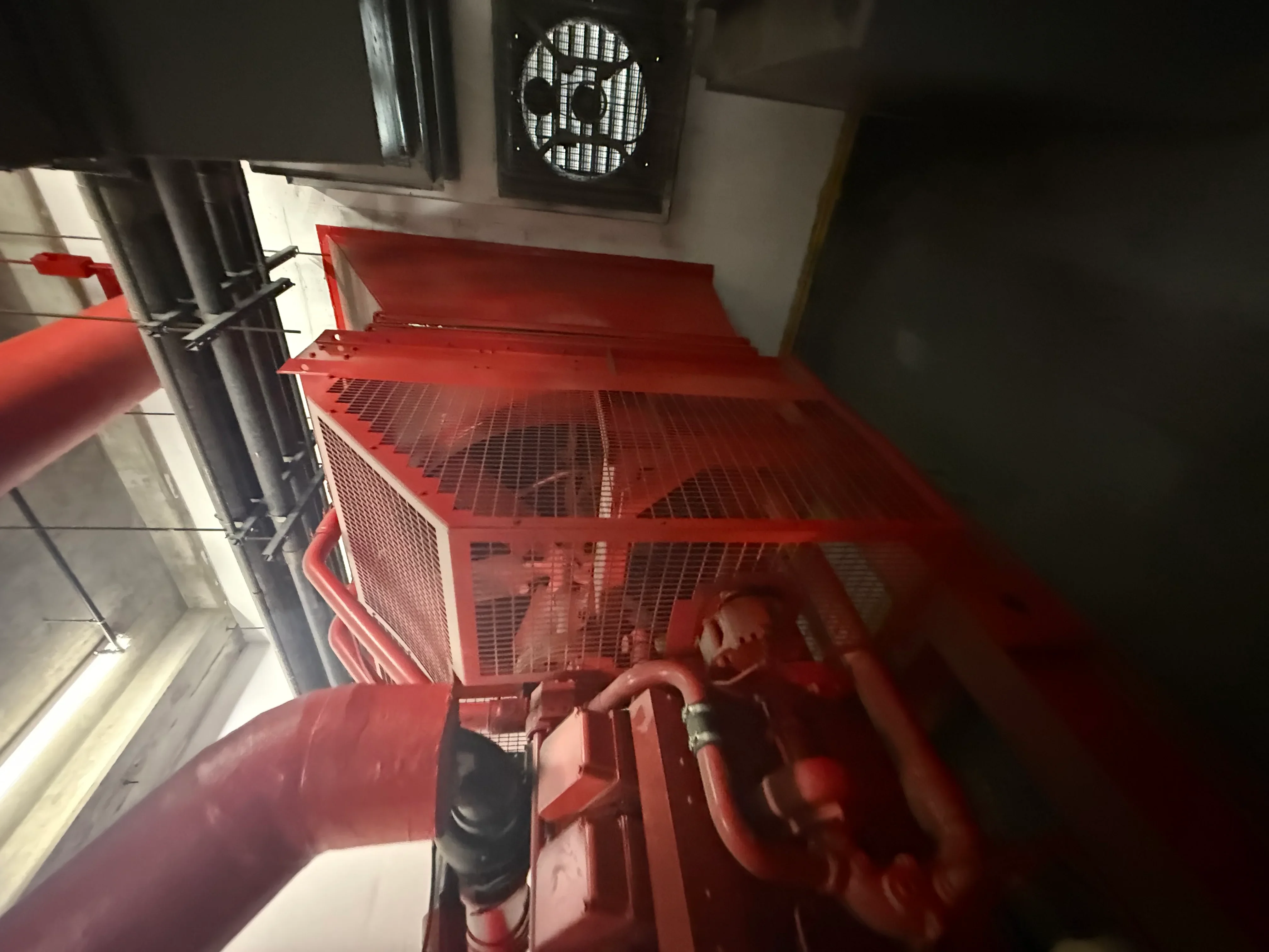 Red industrial generator with mesh panels, piping, and overhead ventilation ducting installed indoors