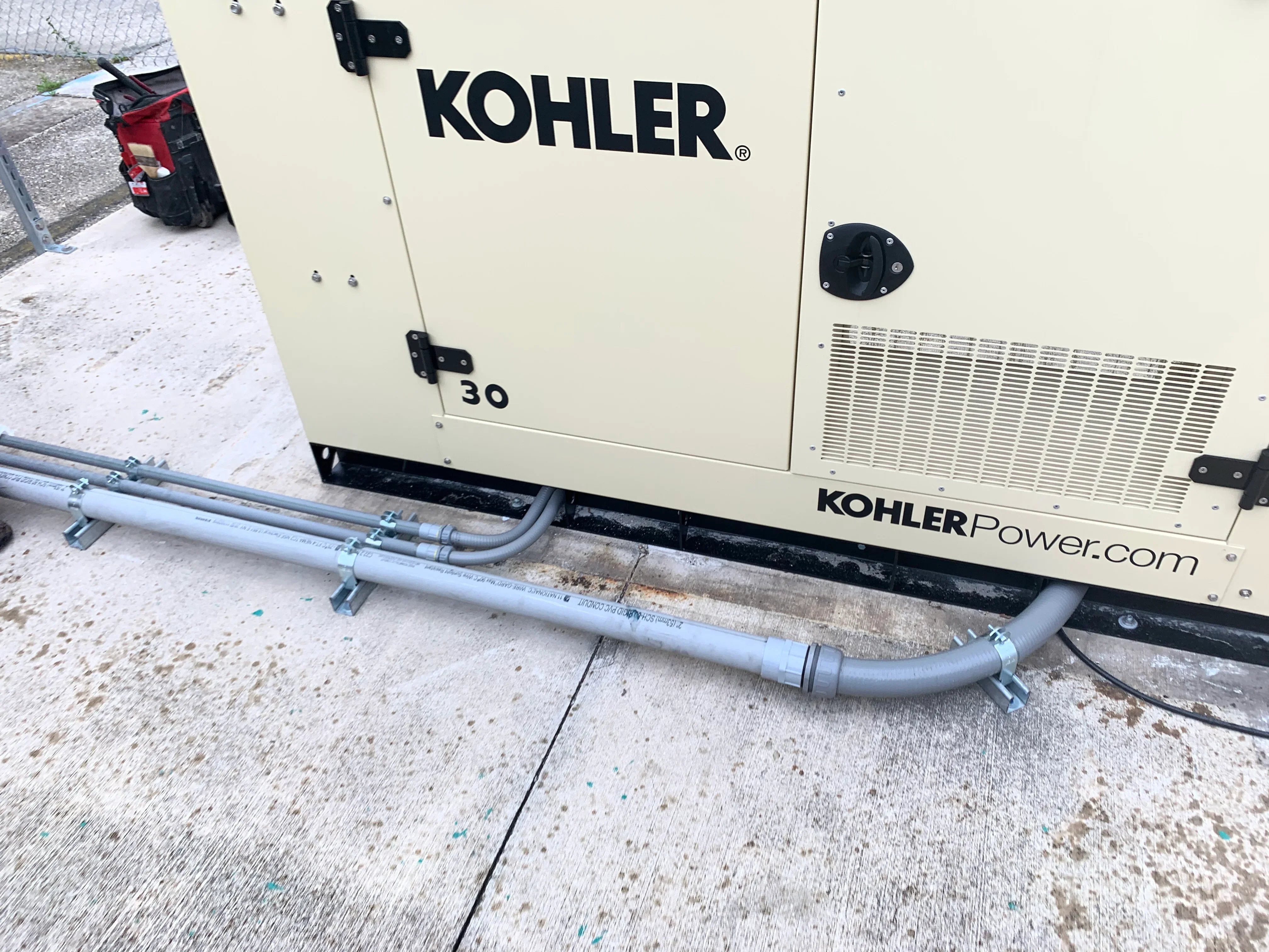 Kohler 30kW generator with gray exhaust piping and support clamps on concrete foundation