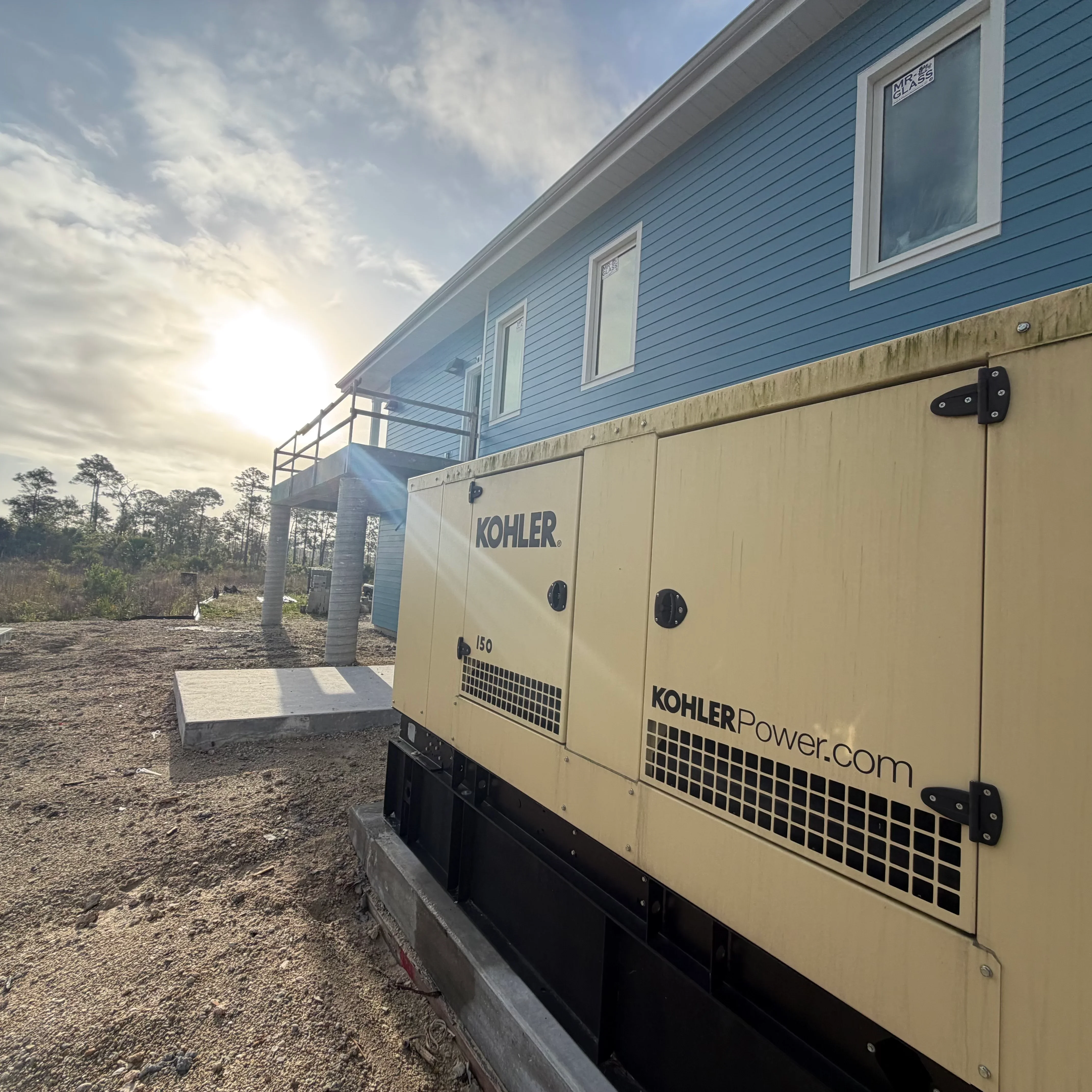 Kohler 150kW diesel generator with tan enclosure installed on concrete pad next to residential building